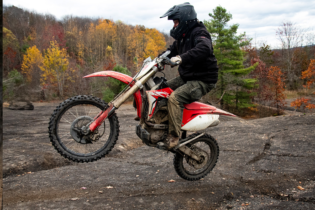 motorcycle flying off a jump at the top of the mountain, fall trees in the background