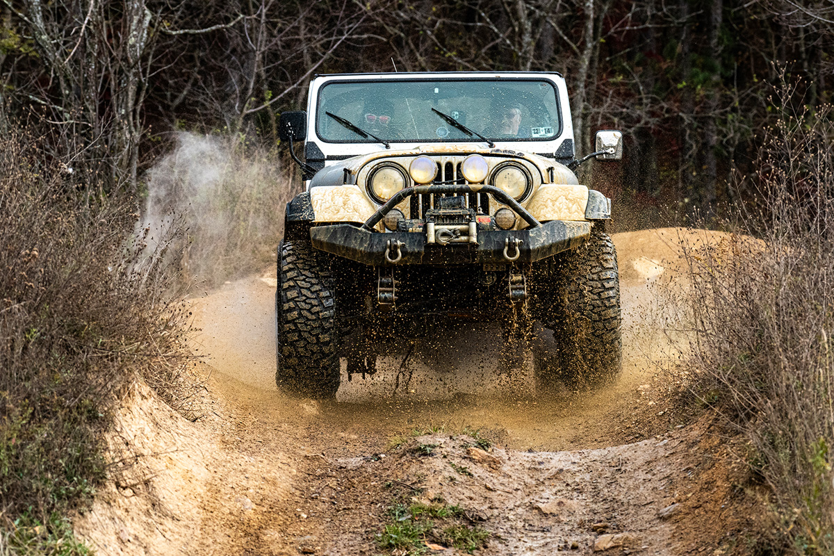 Jeep airborne after plowing through a mud pit, mud is flying everywhere, the driver and passenger are laughing