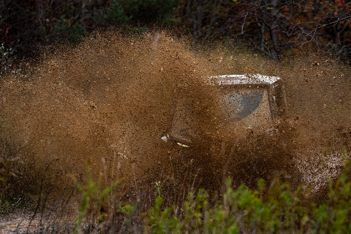 Side-by-side just hitting a mud pit. A wave of mud almost blocks the view of the vehicle it's so thick